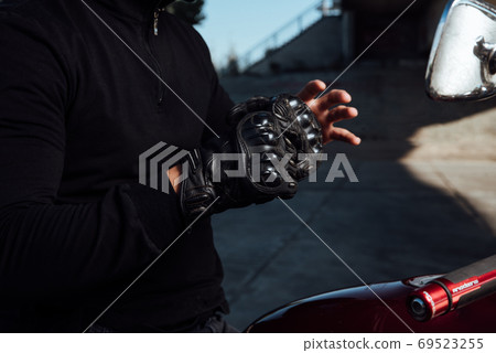 Motorcyclist puts on black leather gloves on hands 69523255