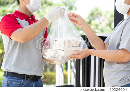 Asian deliverman wearing face mask holding plastic bag with food box delivery to woman customer. 69524004