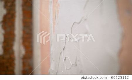master is applying white putty on a wall and smearing by putty knife in a room of renovating house in daytime. White stucco on the wall. Putting plaster on the wall. Repair in the apartment. Applying 69525112