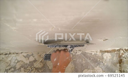 construction notched trowel and worker hands with white mortar on wall. Worker levels a wall with mortar 69525145