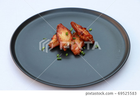 Grilled chicken wings in the black round plate on the white floor. 69525583