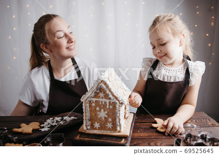 Mother and daughter decorating gingerbread house 69525645