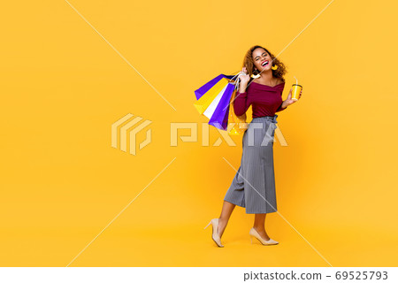 African American woman holding shopping bags and drink cup walking  69525793