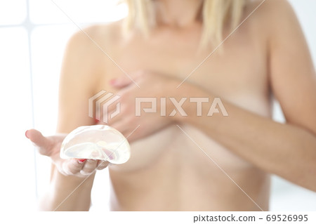 Young woman holds silicone breast implant in hand 69526995