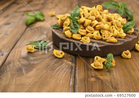 Tortellini mignon on a wooden board with basil and parmesan. Specialties of the cuisine from Bologna 69527600