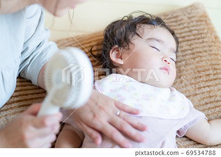 Midsummer Mother's hand hitting a sleeping baby with a handy fan 69534788