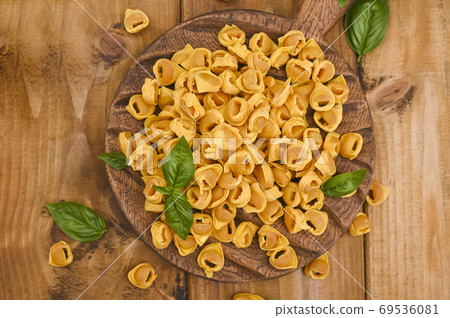 Tortellini mignon on a wooden board with basil and parmesan. Specialties of the cuisine from Bologna Tortellini mignon on a wooden board with basil and parmesan. Specialties of the cuisine from Bologna 69536081