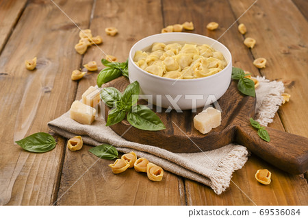 Tortellini mignon on a wooden board with basil and parmesan. Specialties of the cuisine from Bologna Tortellini mignon on a wooden board with basil and parmesan. Specialties of the cuisine from Bologna 69536084