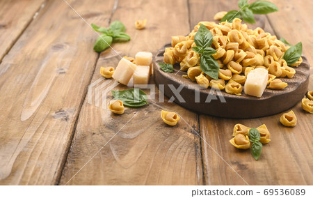 Tortellini mignon on a wooden board with basil and parmesan. Specialties of the cuisine from Bologna 69536089