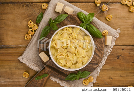 Tortellini mignon on a wooden board with basil and parmesan. Specialties of the cuisine from Bologna 69536091