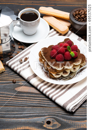 portion of Classic tiramisu dessert with raspberries, cup of espresso and coffee maker on wooden background 69537025