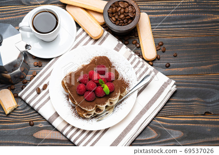 portion of Classic tiramisu dessert with raspberries, cup of espresso and coffee maker on wooden background 69537026