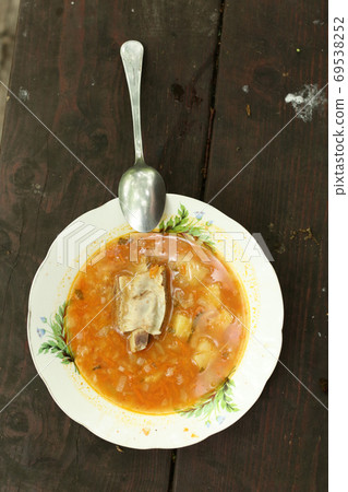 plate with soup containing meat with bone, potato rice and tomato sauce 69538252