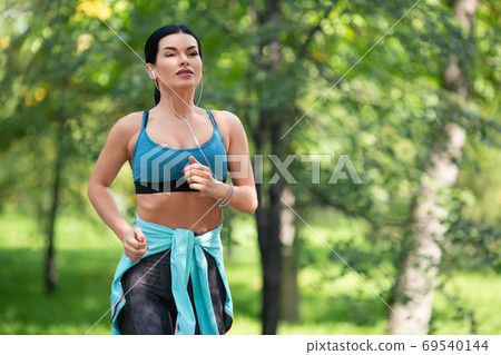 Sportswoman runs along the road in a city park. Sportswoman runs along the road in a city park. 69540144