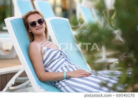 Beautiful woman in sunglasses and striped dress lye on deck chair. Beautiful woman in sunglasses and striped dress lye on deck chair. 69540170