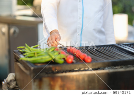 Cook in white coat grill vegetables in summer kitchen. Cook in white coat grill vegetables in summer kitchen. 69540171