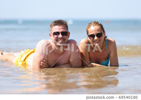 Man and woman in sunglasses lie side by side in water. 69540180