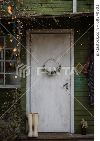 Holiday decorated rustic wooden door with a wreath, old rubber boots and sparkling garland 69540901