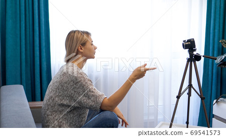 Young woman in casual clothes records herself on camera on tripod. Side view Young woman in casual clothes records herself on camera on tripod. Side view 69541573