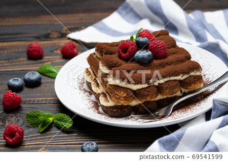portion of Classic tiramisu dessert with raspberries and blueberries on wooden background 69541599