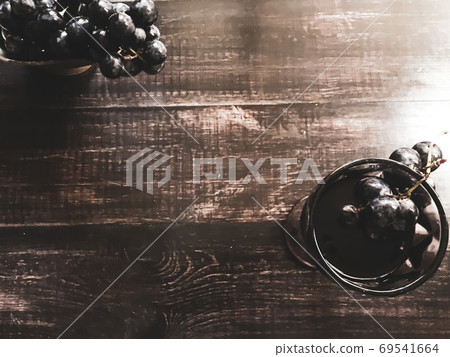 A bunch of grapes in an old vase and in glass for wine with wine a glass of wine on a wooden table . 69541664