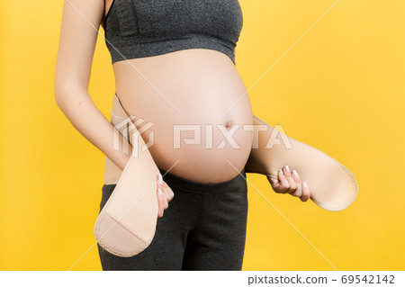 Close up of pregnant woman putting on pregnancy bandage at yello Close up of pregnant woman putting on pregnancy bandage at yello 69542142