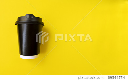 Black paper coffee cup to go on a yellow backgroud. Simple flat lay with copy space. Minimal concept. Stock photo. 69544754