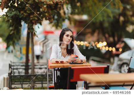 Woman sitting at a table on the street. Evening warm city. Woman sitting at a table on the street. Evening warm city. 69546166