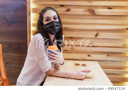 A young woman in a mask from the virus went for coffee. The city is in quarantine. A young woman in a mask from the virus went for coffee. The city is in quarantine. 69547124