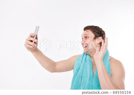 the guy takes a selfie after morning procedures. A man looks at the phone camera. Smooth-shaven face. Blue towel around her neck. Man and modern technologies. the conversation via video link 69550159