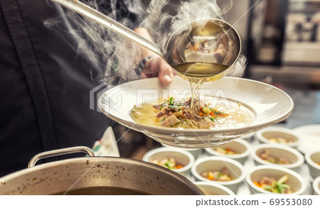 Chef pours broth into a chicken soup with noodles, meat and vegetable Chef pours broth into a chicken soup with noodles, meat and vegetable 69553080