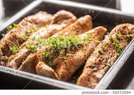 pork fillets in a baking dish seasoned with spices and herbs before baking 69553094