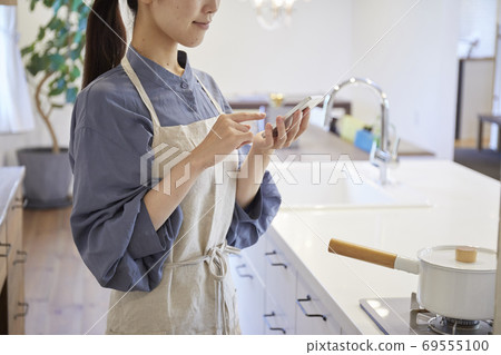A young woman operating home appliances with a smartphone A young woman operating home appliances with a smartphone 69555100