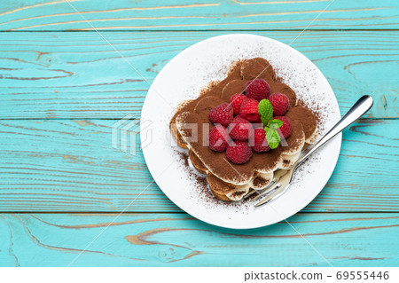 portion of Classic tiramisu dessert with raspberries on blue wooden background 69555446