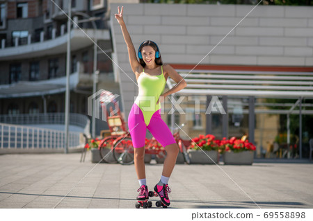 Girl in bright sportswear and roller-skates raising hand in the air Girl in bright sportswear and roller-skates raising hand in the air 69558898