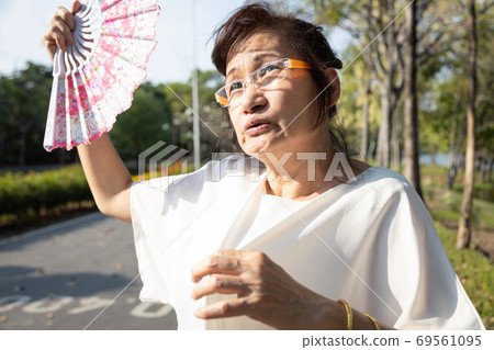 Asian senior woman fanning and sweat on face suffer from sunburn very hot in summer weather problem feel faint, tired female elderly people with heat stroke in the street,high temperature on sunny day 69561095