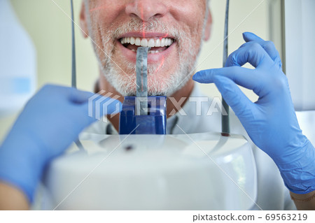 Aging man biting a blocker of a panoramic x-ray machine Aging man biting a blocker of a panoramic x-ray machine 69563219