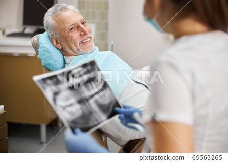 Senior citizen sitting in dental chair looking at a dental technician Senior citizen sitting in dental chair looking at a dental technician 69563265