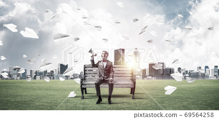 Businessman in summer park announcing something in loudspeaker and paper planes flying around Businessman in summer park announcing something in loudspeaker and paper planes flying around 69564258