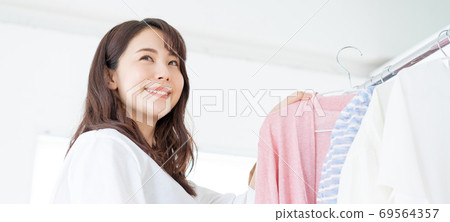 A smiling young woman choosing clothes banner size A smiling young woman choosing clothes banner size 69564357