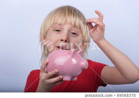 Boy puts coin into piggy Bank. Child learns to save money. Boy puts coin into piggy Bank. Child learns to save money. 69568378