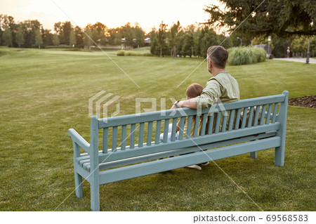 Rear view of father and little daughter sitting on the wooden bench in nature, spending time together in park. 69568583