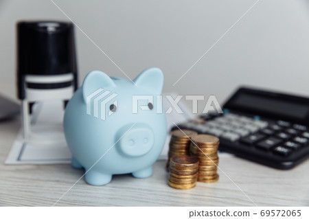 Blue piggy bank, stamp and coins on wooden desk in office. Save money and management financial concept 69572065
