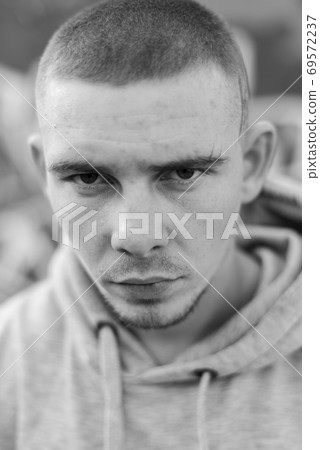 A bully guy in a light sports jacket with a hood. Black and white photo. BW A bully guy in a light sports jacket with a hood. Black and white photo. BW 69572237