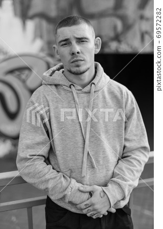 A bully guy in a light sports jacket with a hood. Black and white photo. BW A bully guy in a light sports jacket with a hood. Black and white photo. BW 69572282