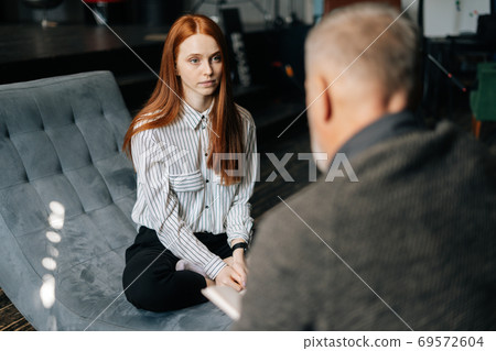 Unrecognizable mature gray-haired man sits in front of young red-haired woman in office Unrecognizable mature gray-haired man sits in front of young red-haired woman in office 69572604