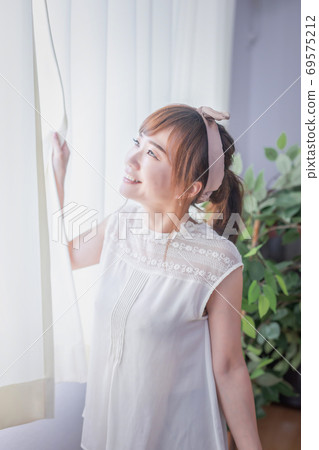 A young woman bathing in the morning sun shining through the curtain 69575212