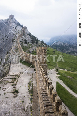 The wall that runs along the ridge of the mountain and the towers of Genoese fortress of the 14th century in the Sudak bay on the Peninsula of Crimea The wall that runs along the ridge of the mountain and the towers of Genoese fortress of the 14th century in the Sudak bay on the Peninsula of Crimea 69577088