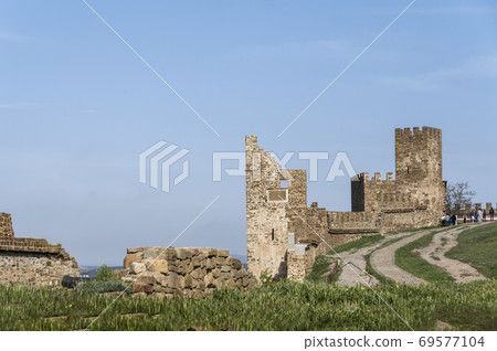 Tower and wall of Genoese fortress of 14th century in the Sudak bay on the Peninsula of Crimea on the background of mountains and cloudy sky Tower and wall of Genoese fortress of 14th century in the Sudak bay on the Peninsula of Crimea on the background of mountains and cloudy sky 69577104