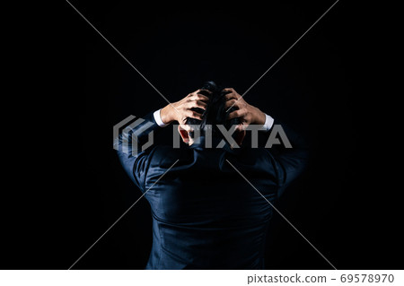 A businessman holding his head in a black background 69578970